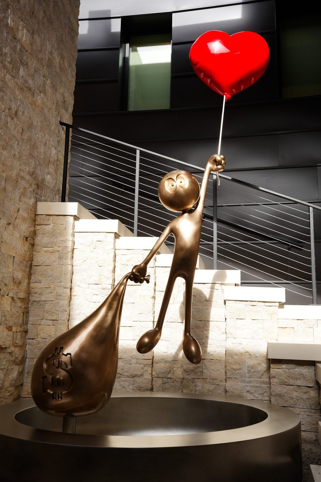 Love vs Money Monumental by Kaï, 2024: a bronze figure lifting a heart balloon, installed outdoors in front of a building