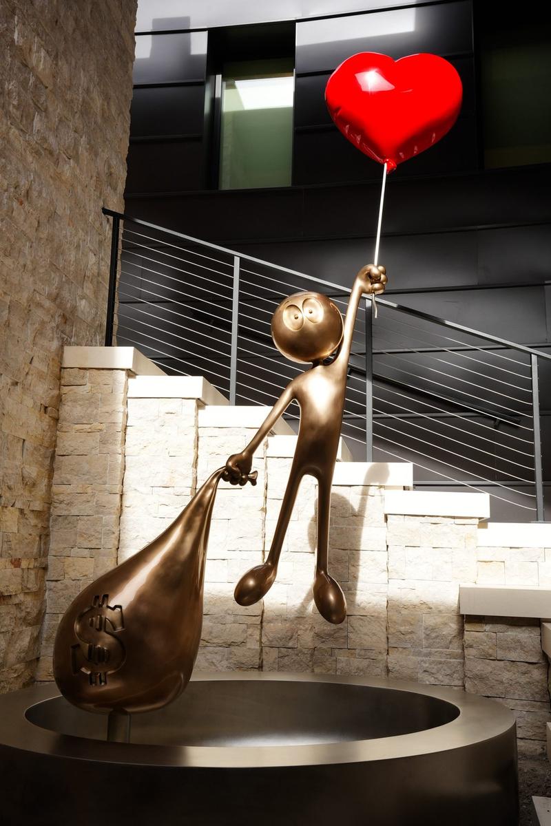 Love vs Money Monumental by Kaï, 2024: a bronze figure lifting a heart balloon, installed outdoors in front of a building