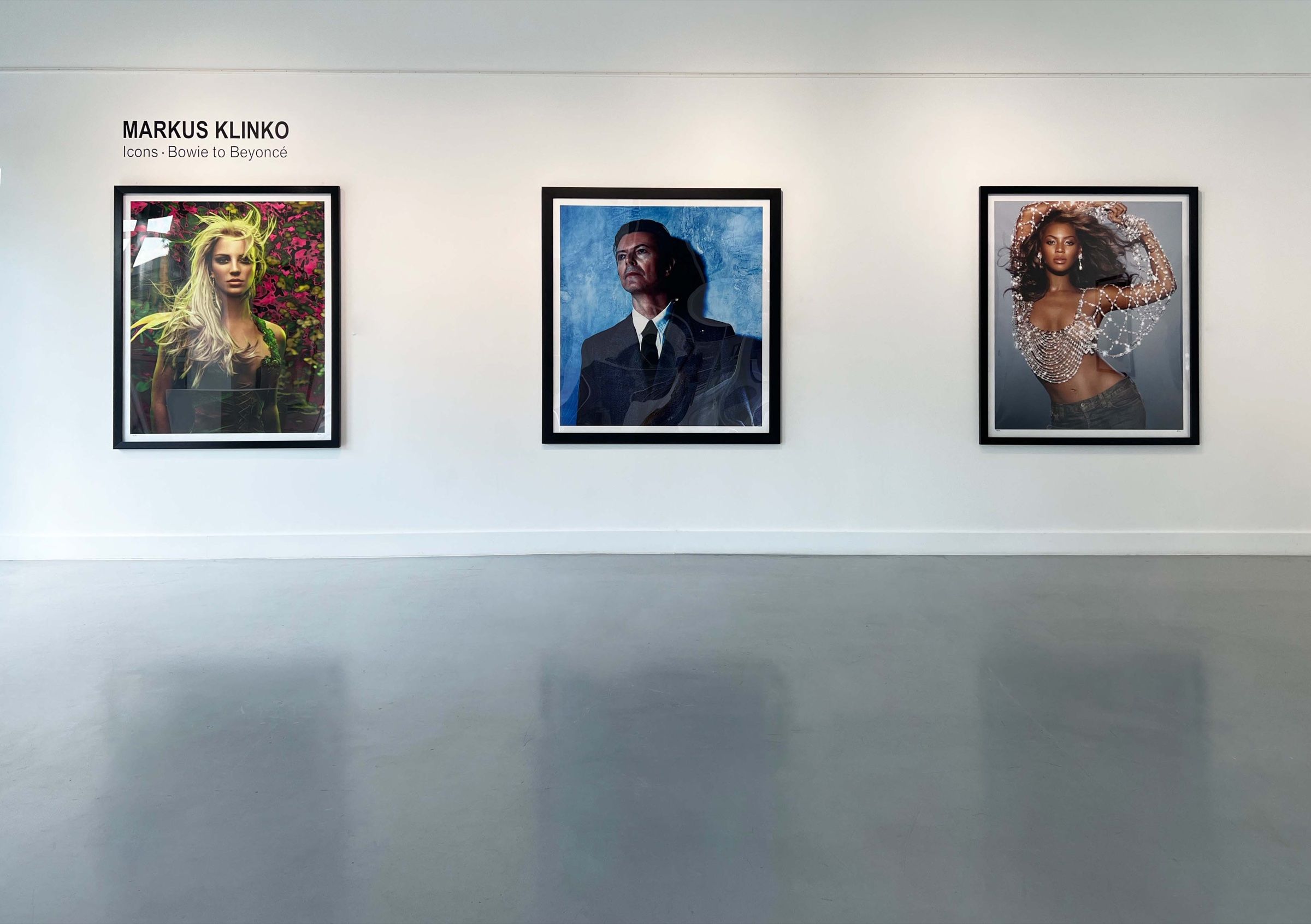Gallery wall titled Markus Klinko, Icons · Bowie to Beyoncé, with three framed photographs: Britney Spears among pink flowers, David Bowie in a dark suit against a blue background, and Beyoncé in a crystal top