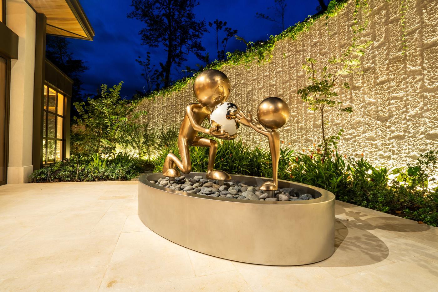 Love vs Money Monumental by Kaï, 2024 — a bronze figure lifting a red heart balloon and dragging a money bag, in front of a stone staircase
