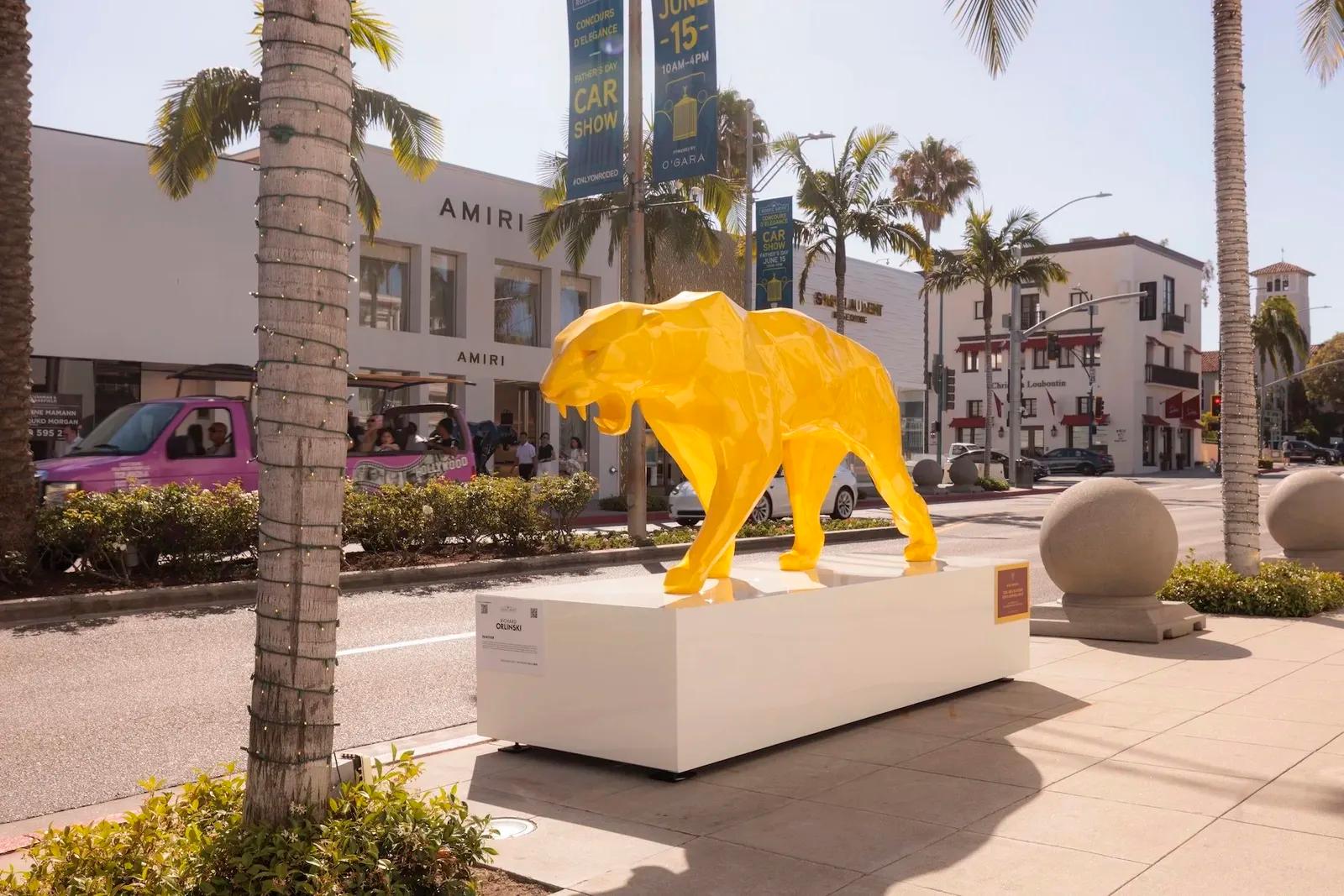 Yellow faceted panther sculpture by Richard Orlinski on a white plinth along Rodeo Drive in Beverly Hills, palm trees and storefronts behind